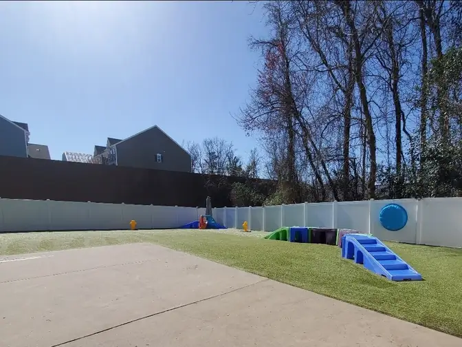 Outdoor dog play yard with artificial turf and play equipment at One Lucky Pup Charlotte