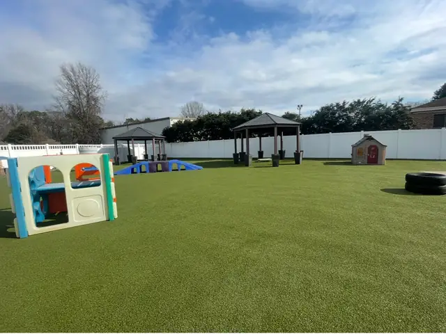 Spacious artificial-turf dog play yard with shade structures and play equipment at One Lucky Pup Northlake